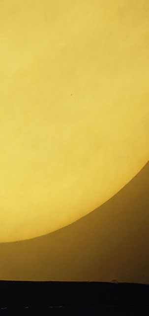 A tiny dot in front of the massive yellow sun